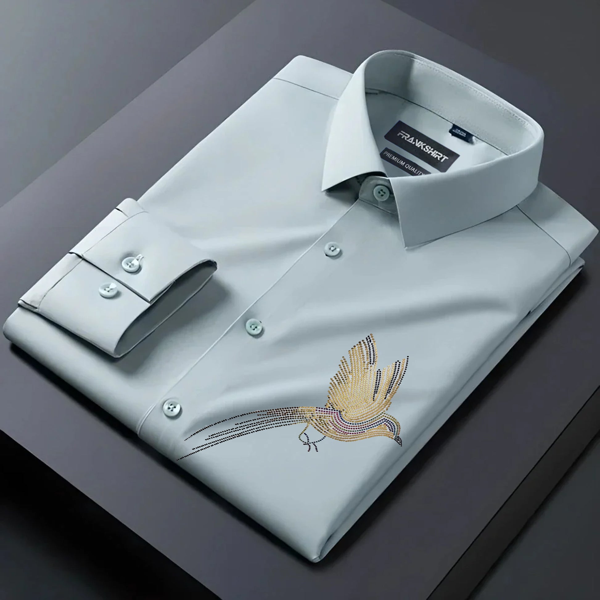 Folded light blue dress shirt with bird embroidery on a dark surface