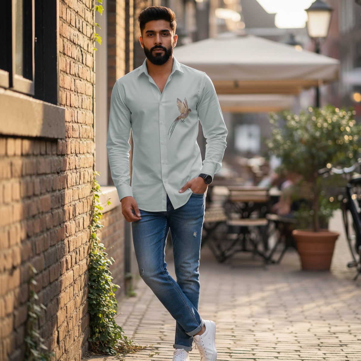 Man walking along a street with a brick wall and outdoor seating in the background